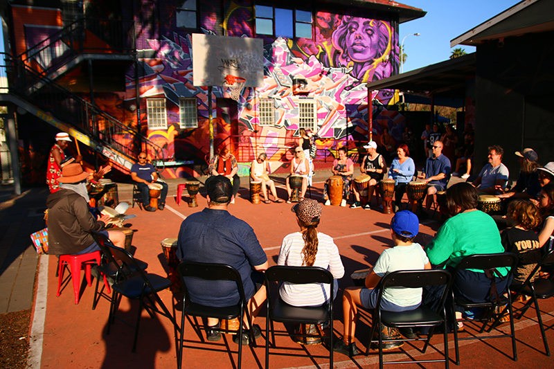 A large circle of seated people playing drums.